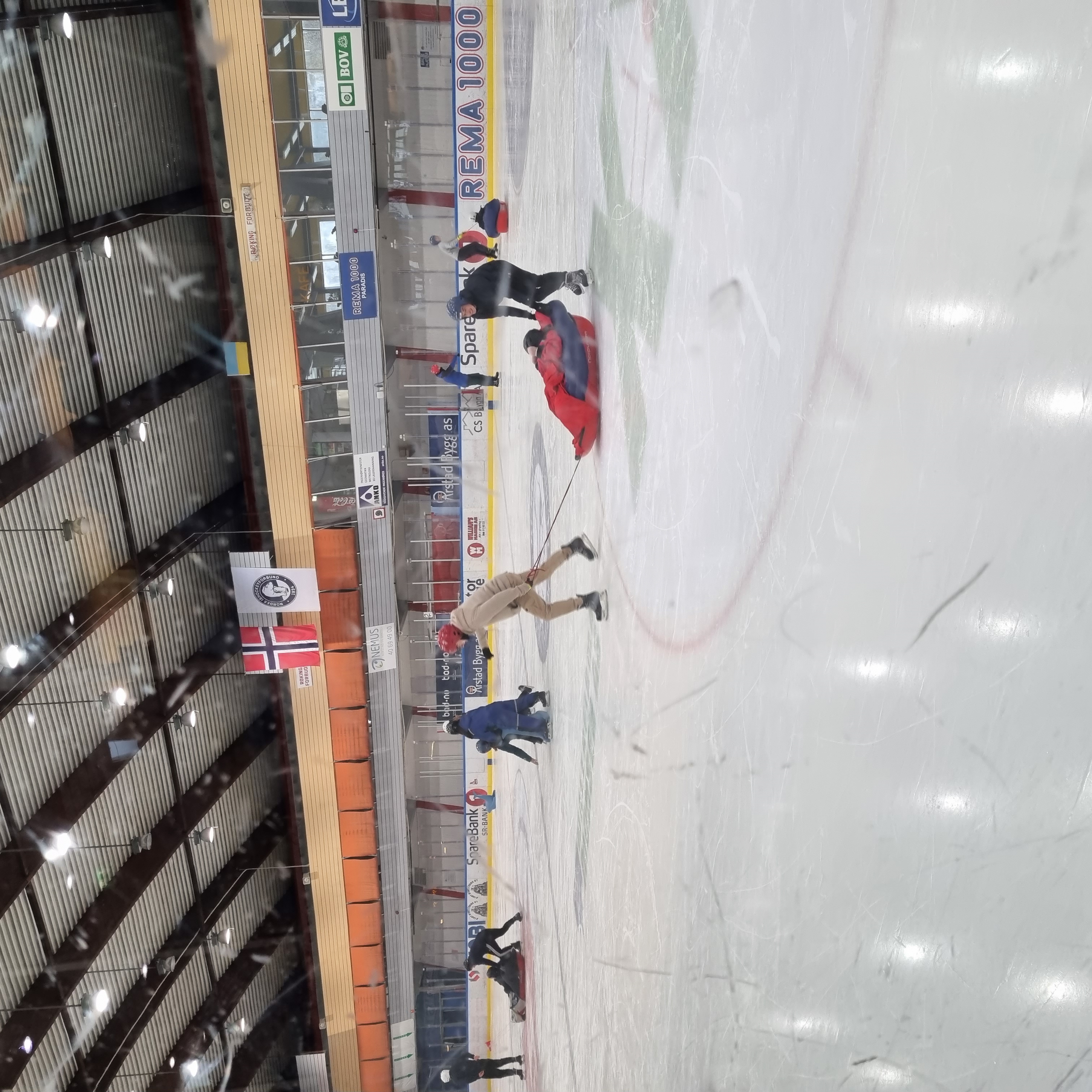 En person sitter i en pulk og blir trukket av to personer rundt på isen